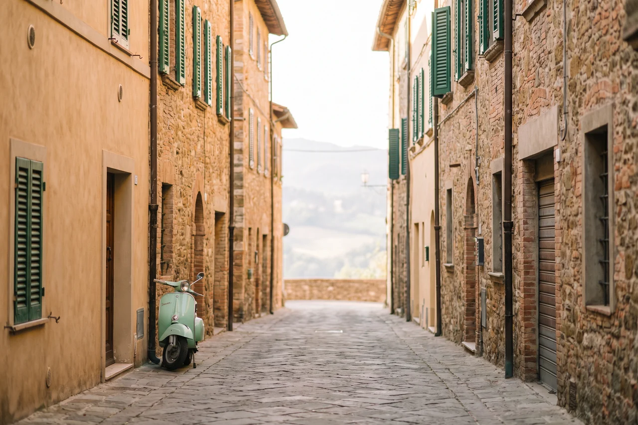 Una stretta via di un paese italiano con le case in pietra, le persiane verdi e una Vespa parcheggiata vicino al muro