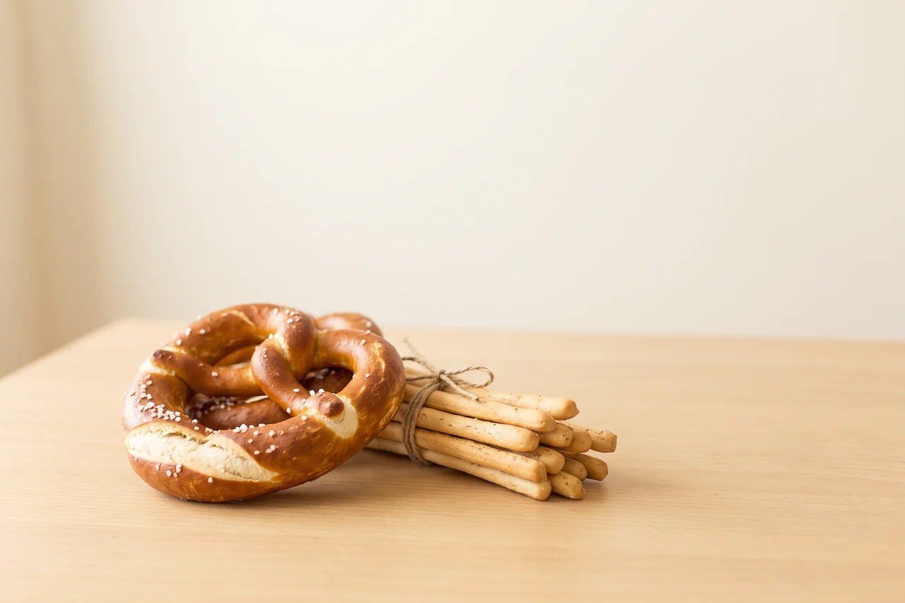 Eine deutsche Brezel und italienische Grissini nebeneinander auf einem Holztisch