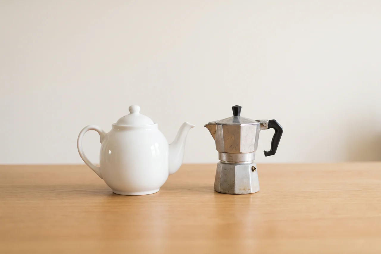 An English teapot and an Italian moka coffee pot side by side on a wooden table