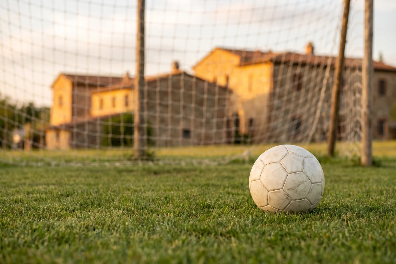 Un pallone da calcio sull’erba davanti alla rete della porta, con le case di un paese italiano sfocate sullo sfondo
